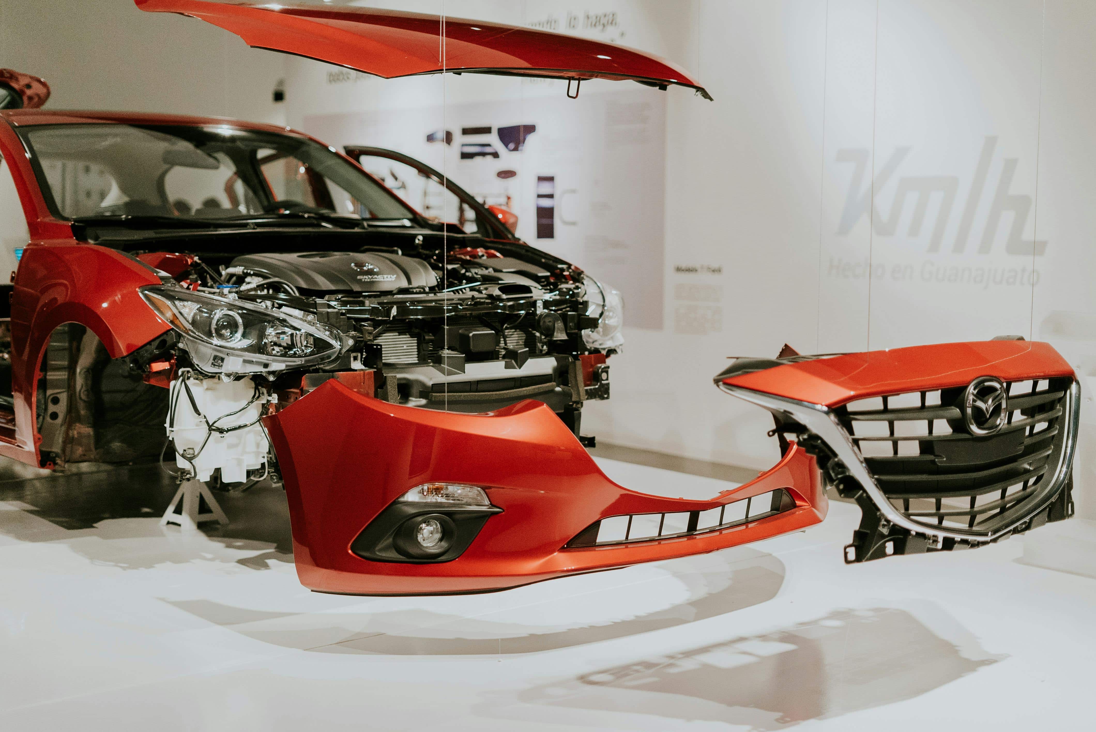 Explore a detailed view of a partially disassembled red Mazda 3 showcased at an auto exhibition.